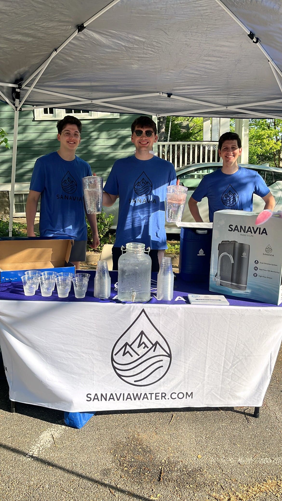 The Sanavia team at their booth at the Arlington Bunny Hop, behind a SanaviaWater.com banner pouring filtered water